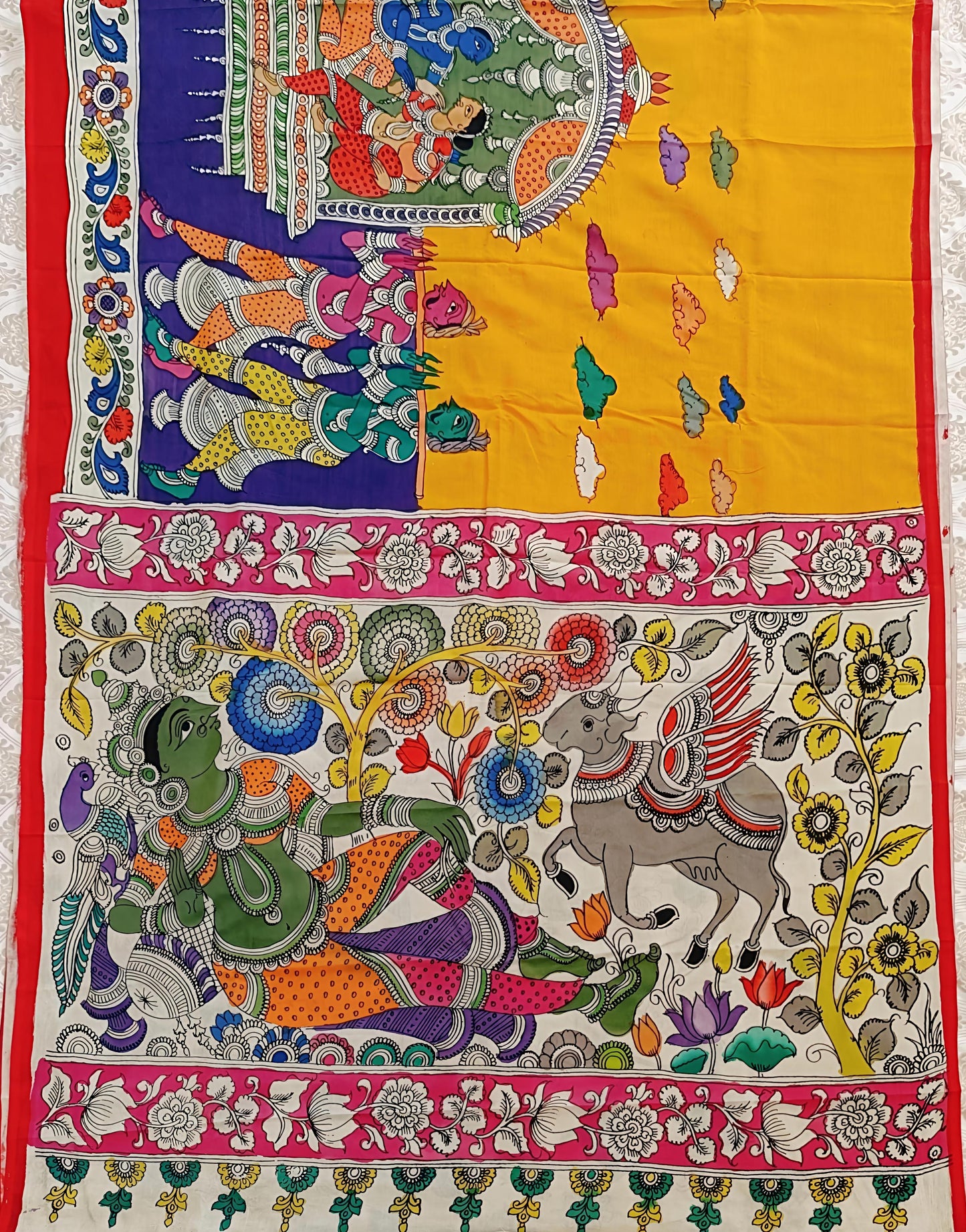 Colorful tapestry with intricate designs of elephants and other elements on a yellow background.