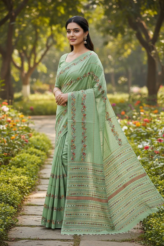Woman in a green saree with floral patterns standing in a garden.